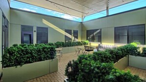 Une cour intérieure avec un sol en briques, des jardinières vertes et un espace détente comprenant des chaises et des tables.