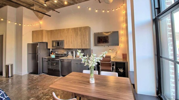 Une cuisine moderne avec des meubles en bois, des appareils électroménagers en acier inoxydable et un coin repas comprenant une table et des chaises en bois.