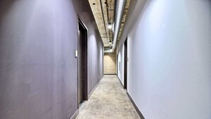 Un couloir doté d’un sol en béton, de murs gris et d’un plafond apparent avec des tuyaux exposés.