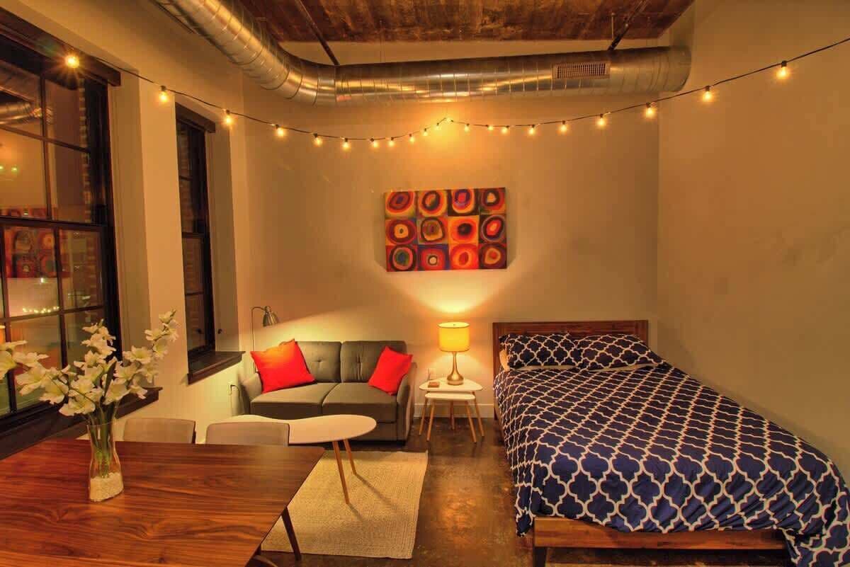 Una habitación acogedora con una cama, un sofá, una mesita y un jarrón de flores.