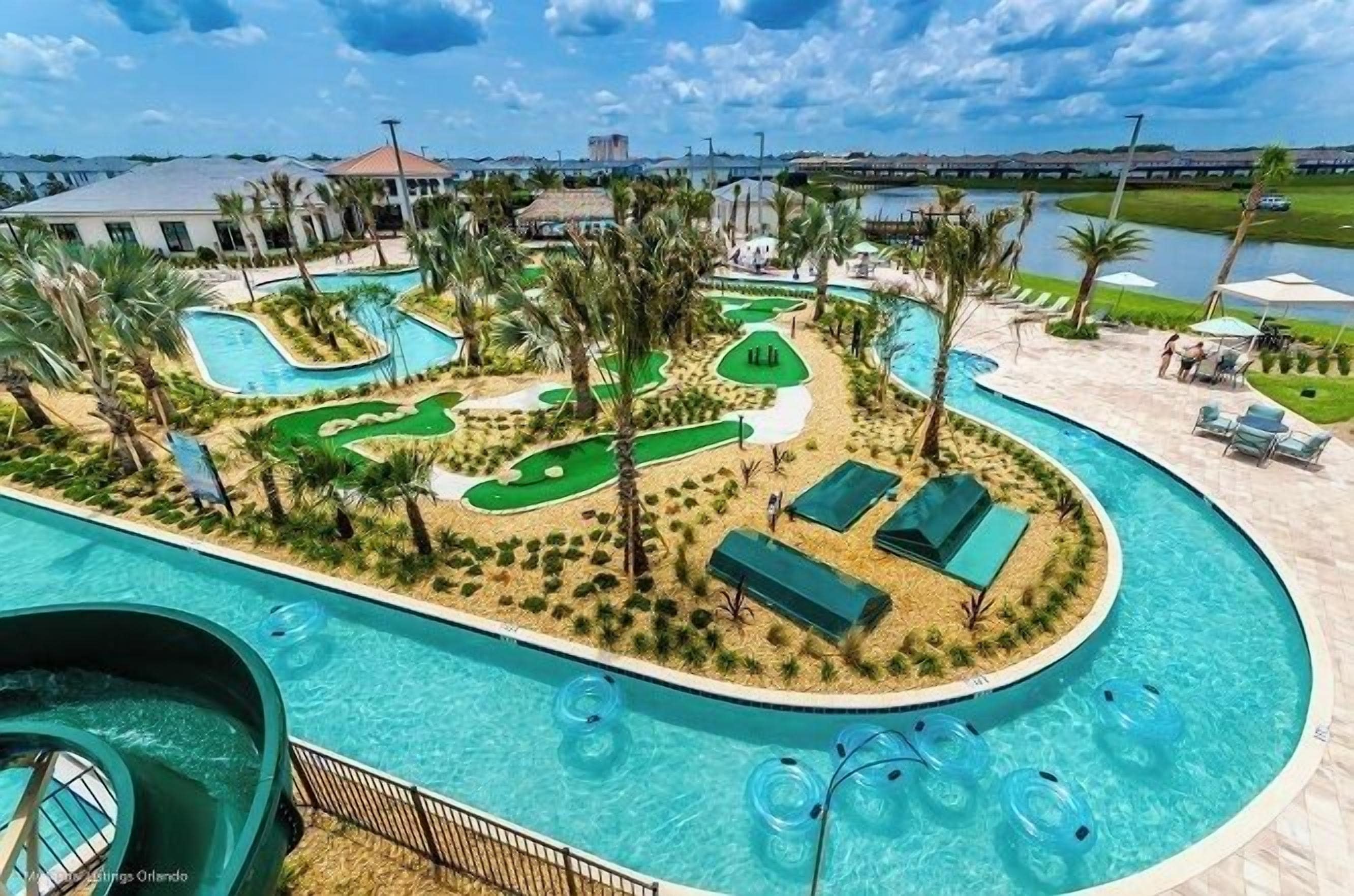 Un área de piscina con tobogán de agua, sillas de descanso y palmeras.