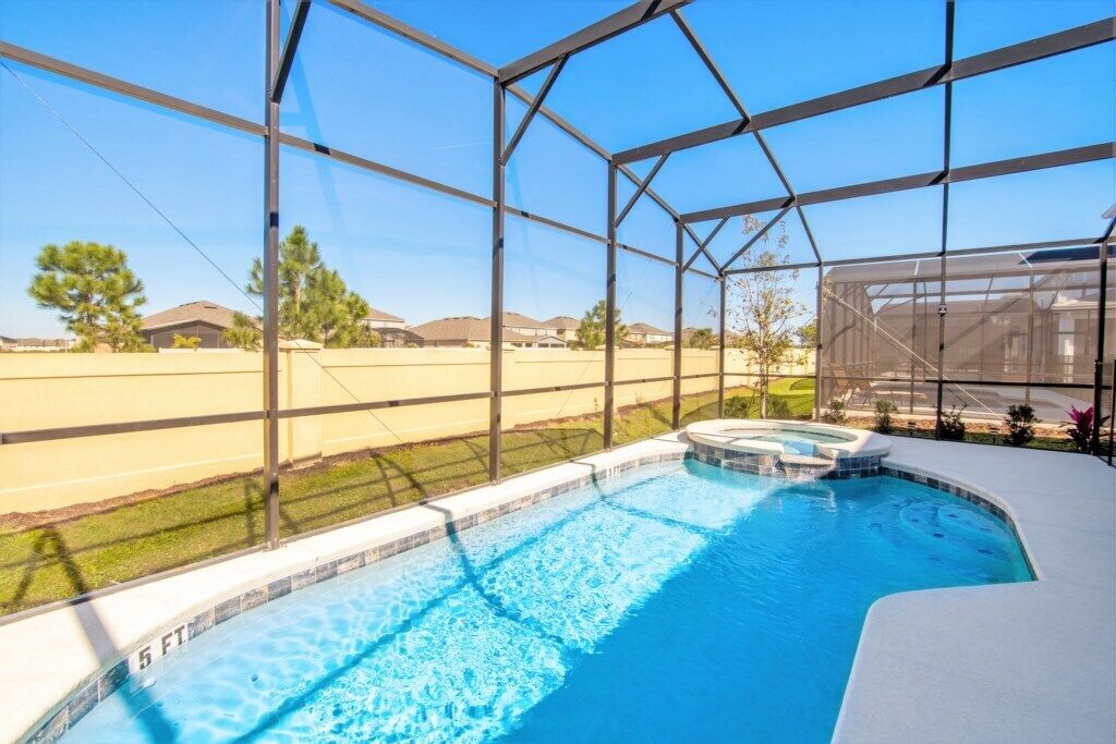 A swimming pool with a hot tub, surrounded by a covered area with large windows.