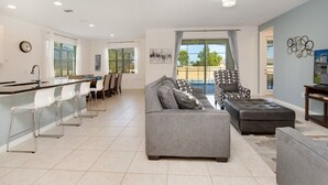 Una sala moderna con un sofá gris, un sillón estampado y un comedor con sillas blancas.