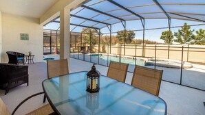 Un patio techado con una mesa de vidrio, sillas de mimbre y un farol. Al fondo, se observa una piscina y un jacuzzi.