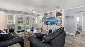 Ein modernes Wohnzimmer mit Flachbildfernseher, dunklen Sofas, einem Couchtisch und einem Deckenventilator.