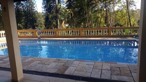 A swimming pool with a wooden fence, surrounded by trees and a tiled deck.