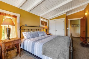A bedroom with a bed, nightstands, a lamp, a window with curtains, and a door.