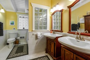 A bathroom with a toilet, sink, vanity, and a window with frosted glass.
