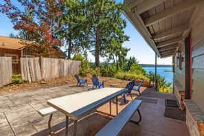 An outdoor patio with a table and chairs, a wooden fence, and a view of the sea.