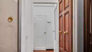 Un pasillo con una puerta blanca, una puerta de madera y un aldabilla de bronce.
