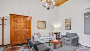 Una sala de estar con sofá, sillas, un aparador de madera, una araña y un tapiz estampado.