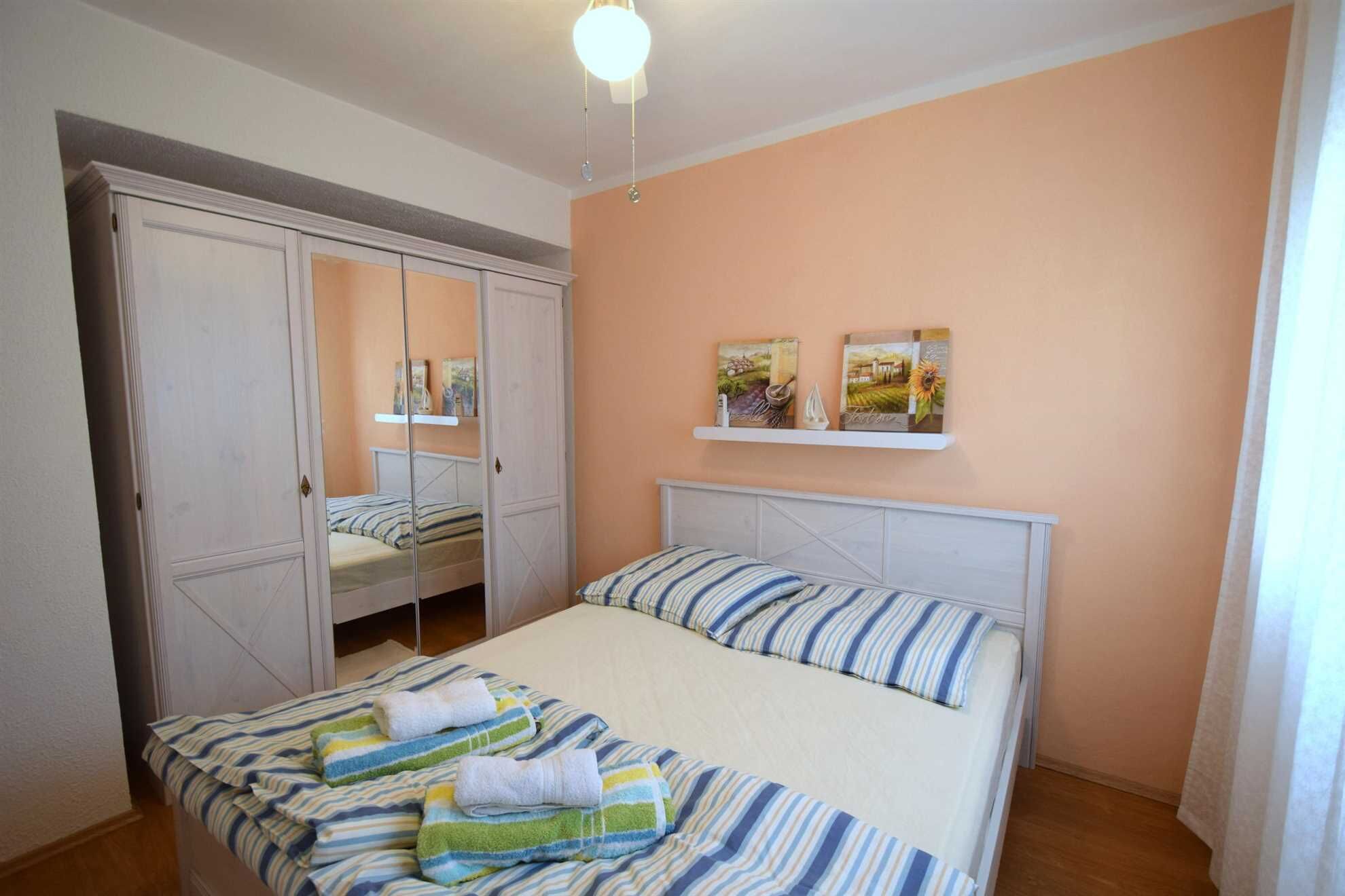 Een slaapkamer met een bed, een kledingkast en twee wandplanken met kunstwerken.