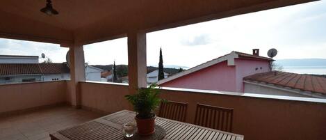 A balcony with a table, chairs, and a potted plant.