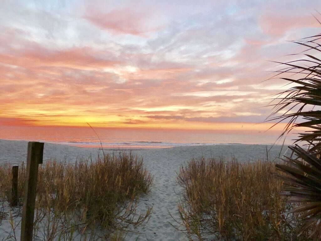 A beach path leading to the ocean with a sunset in the background.