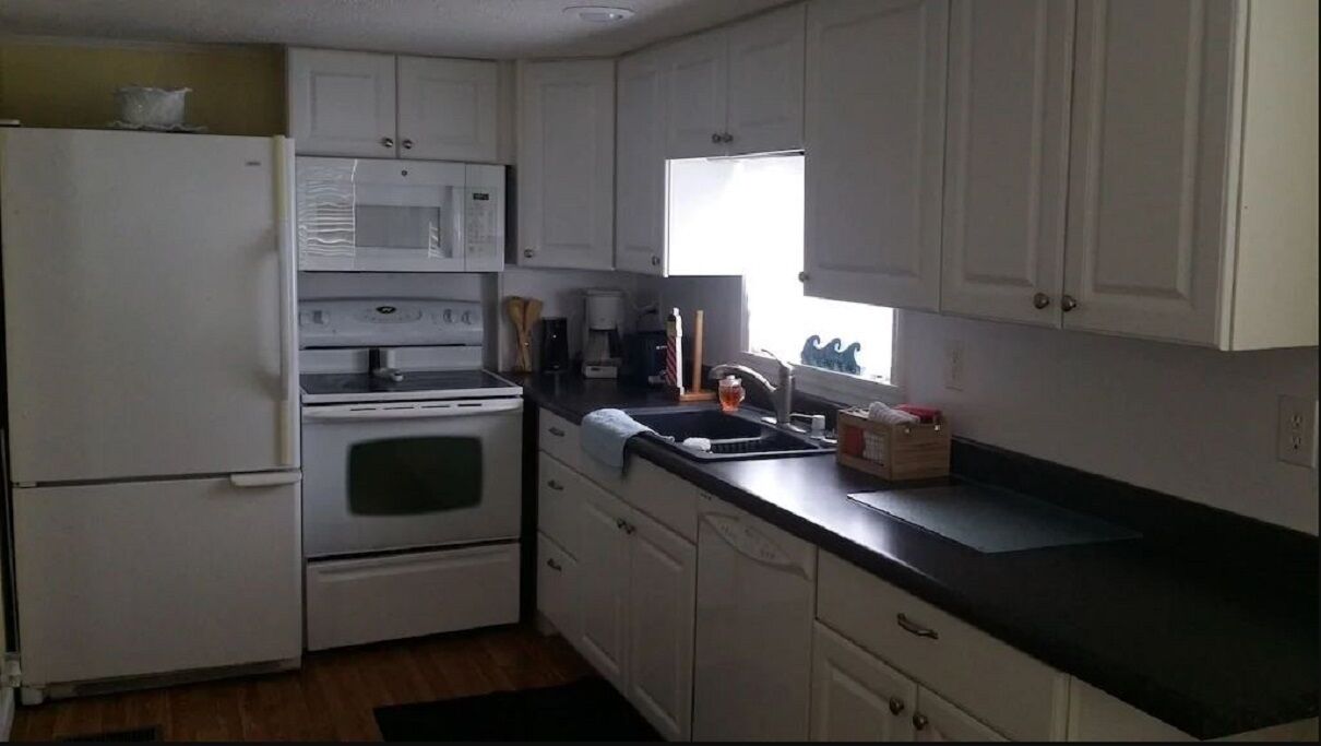 A compact kitchen with white cabinets, a black countertop, and a window providing natural light.