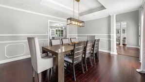 A dining room with a wooden table and chairs, a pendant light, and a view of the kitchen.