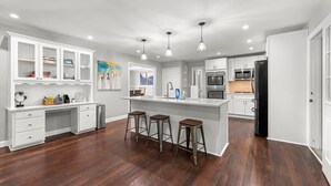 A modern kitchen with white cabinetry, a central island with stools, stainless steel appliances, and recessed ceiling lighting.