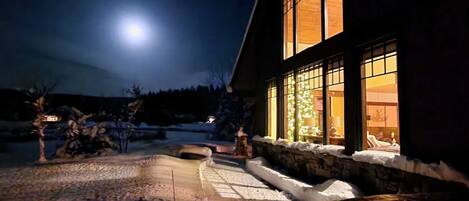 A house with large windows and a snow-covered yard at night.