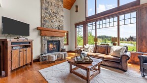 Un salón amplio con chimenea de piedra, un ventanal con vistas al exterior, un sofá de cuero y una mesa de centro de madera.