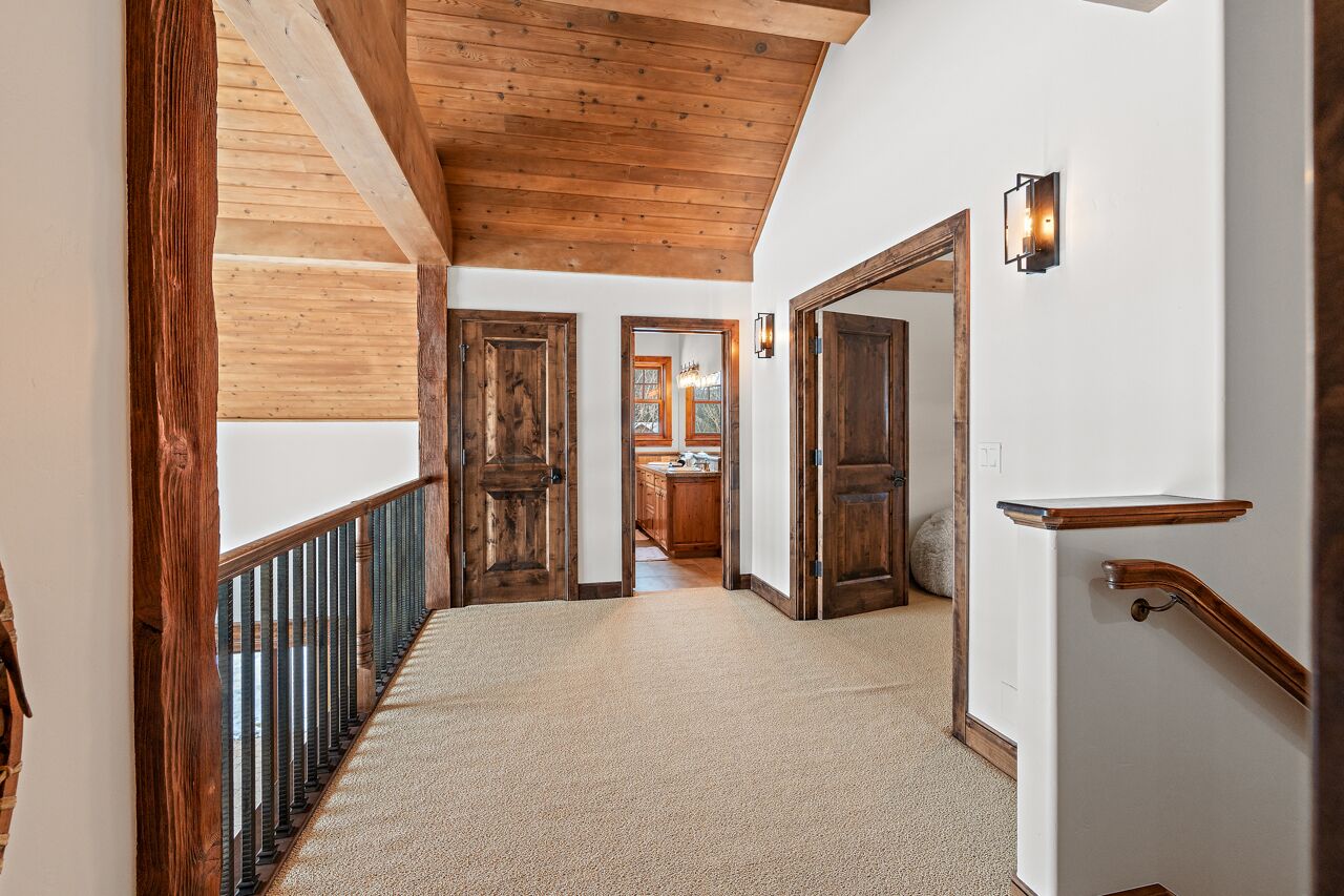A hallway with wooden beams, a carpeted floor, and wooden doors leading to a kitchen area.