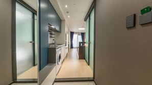 A modern hotel corridor with a kitchen area, including a washing machine, and a view into a room with a bed and curtains. - Risen Oceanpark Hotel (Sokcho)