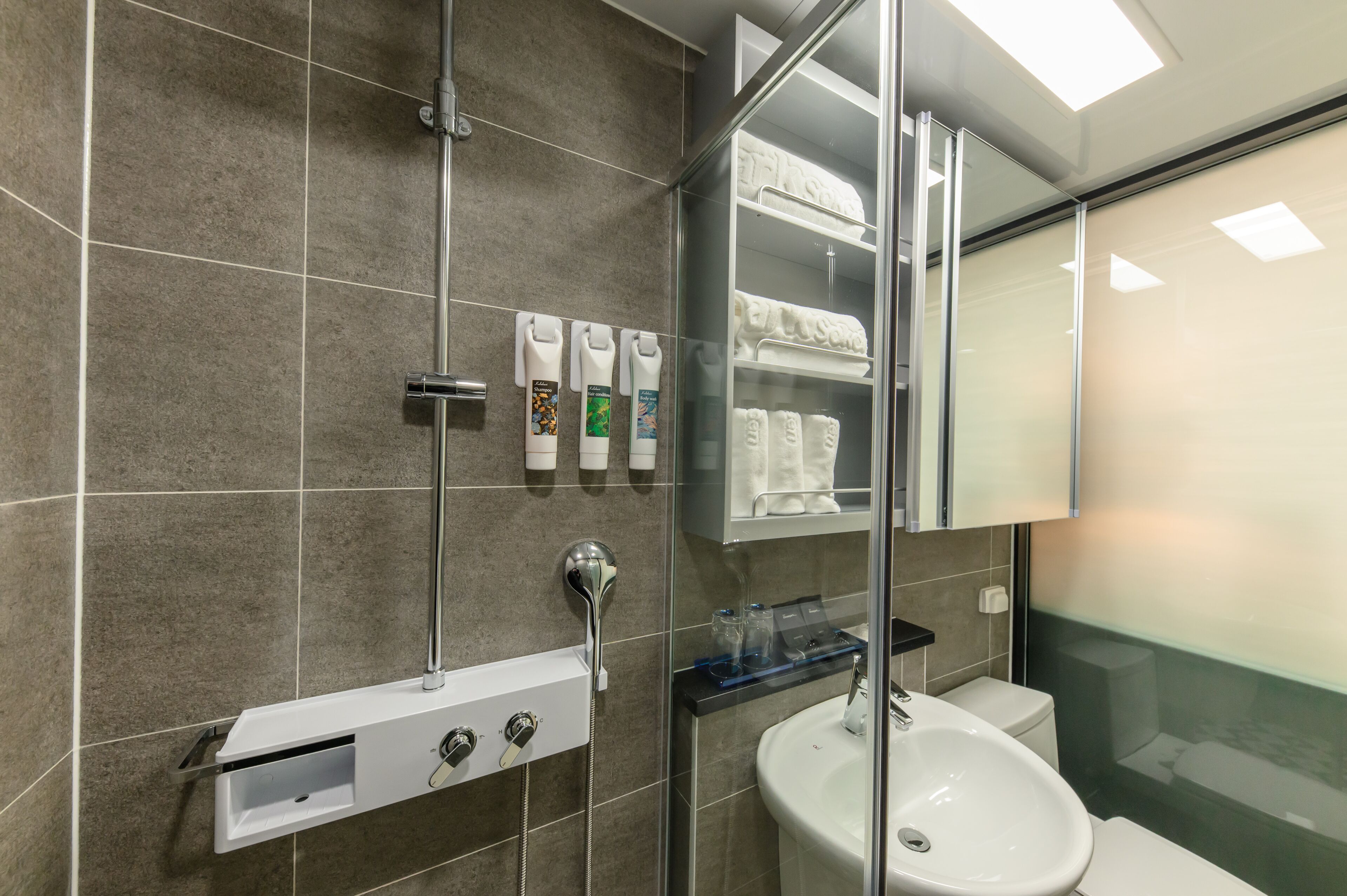 A modern bathroom with a glass shower enclosure, a white sink, and a glass-topped vanity.