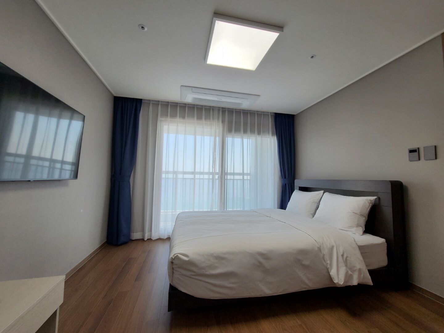 A modern hotel room with a large bed, a flat-screen TV, and a skylight.