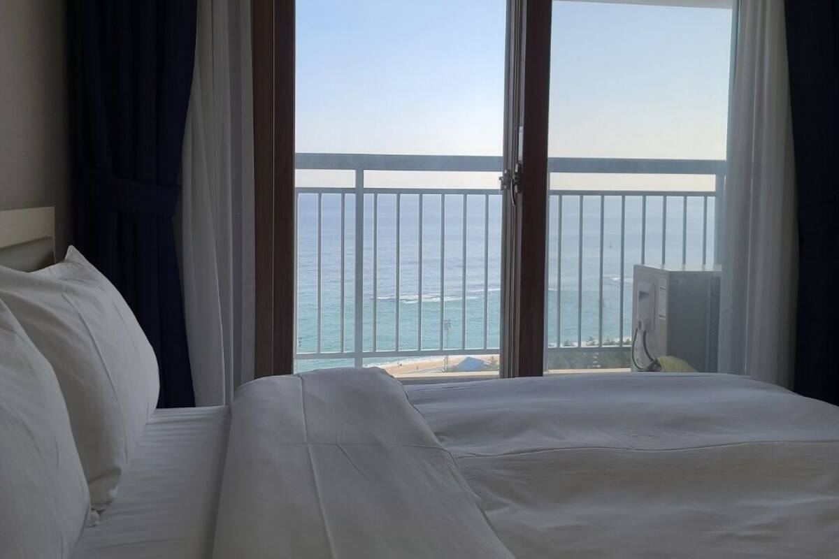 Quarto de hotel com uma cama grande, vista para o oceano e varanda com guarda-corpo.
