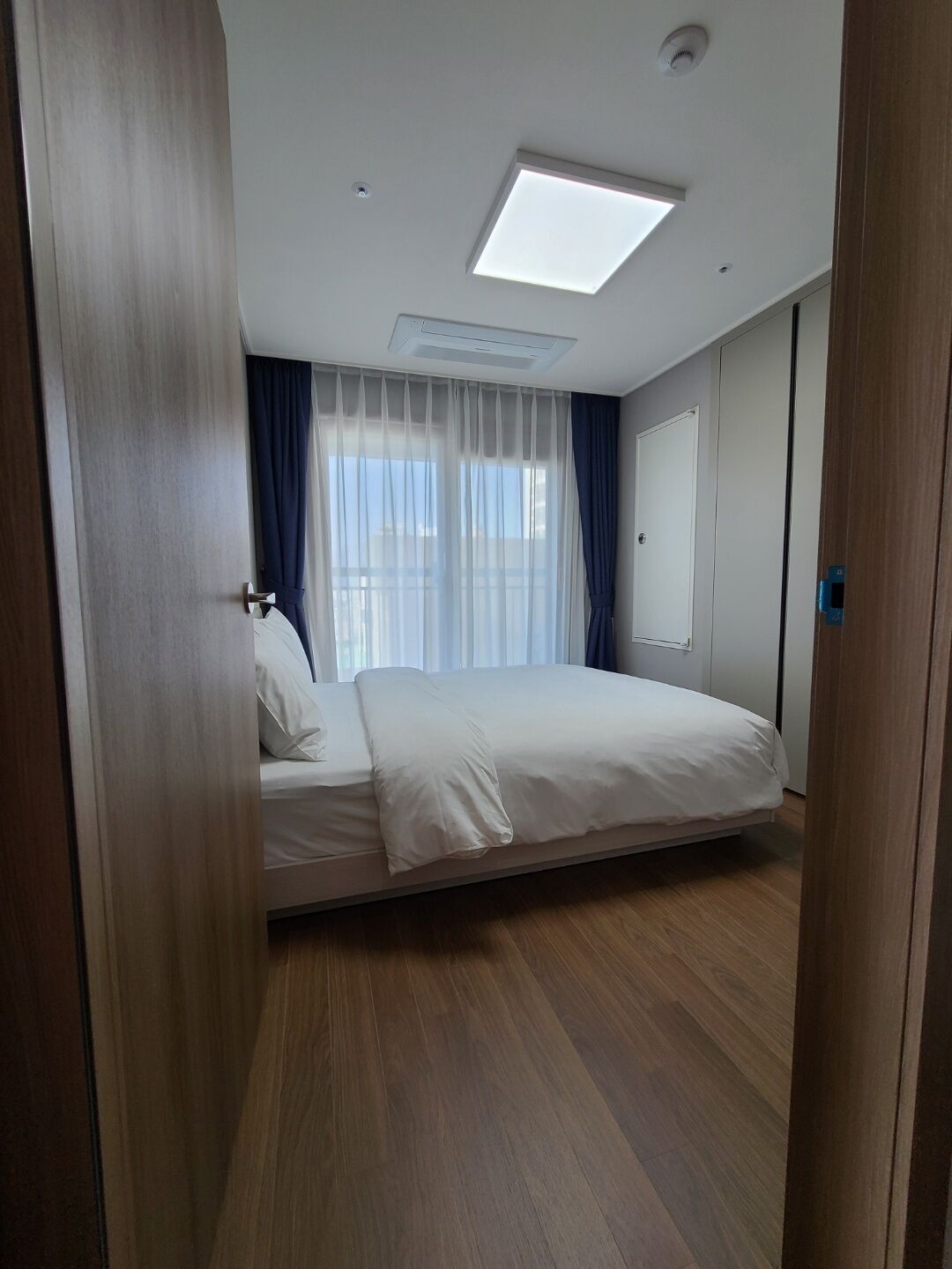 Un dormitorio con cama, una lámpara en el techo y una ventana con cortinas.