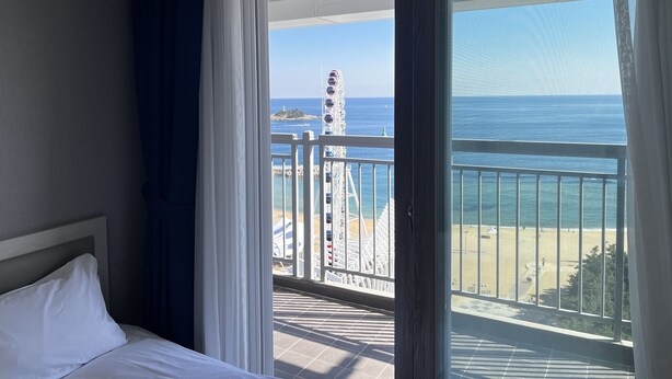 A hotel room with a balcony overlooking a beach and a Ferris wheel. - Risen Oceanpark Hotel (Sokcho)