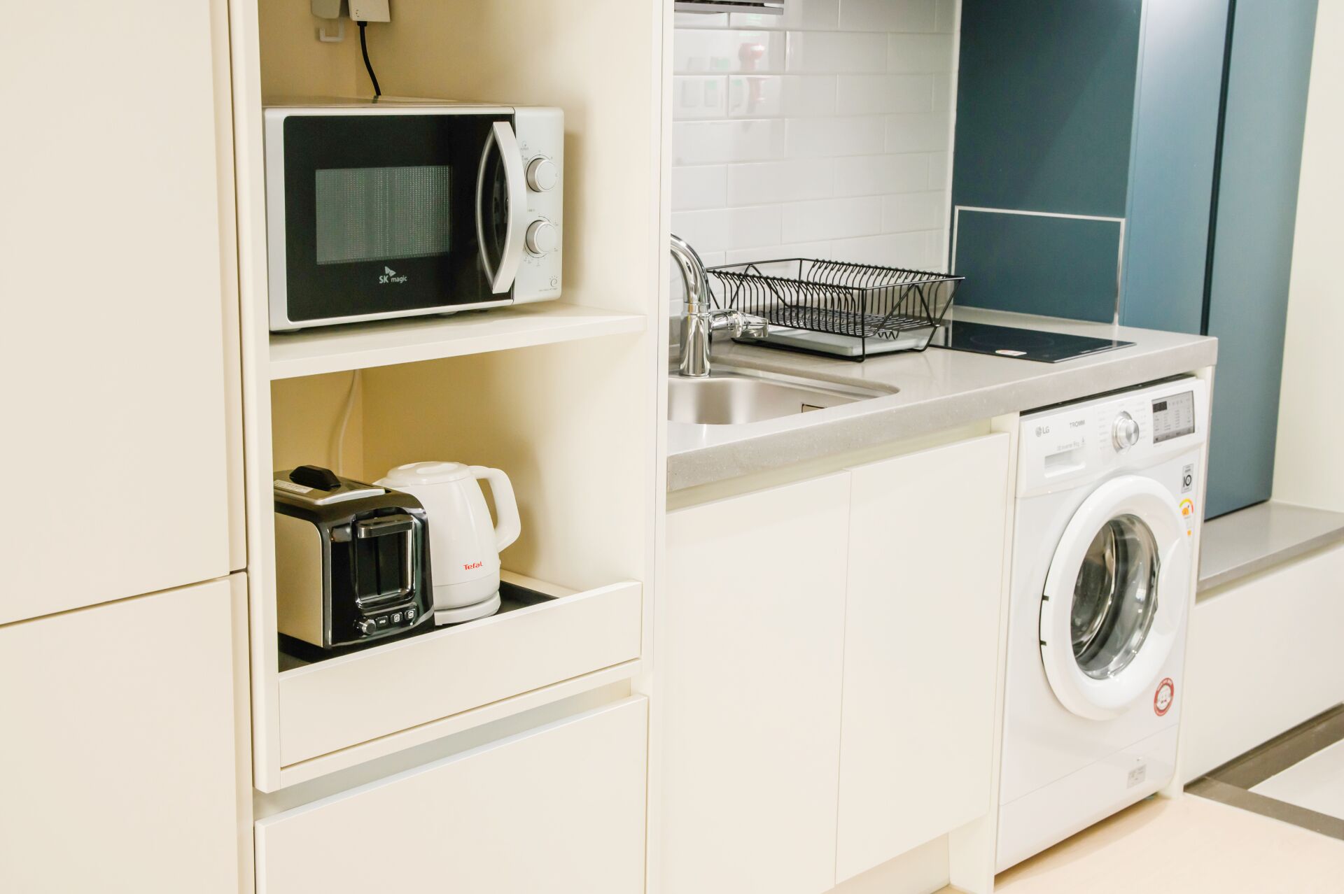 A compact kitchenette with a microwave, toaster, sink, and washing machine.