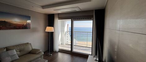 A modern hotel room with a balcony, a sofa, a standing lamp, and a flat-screen TV.
