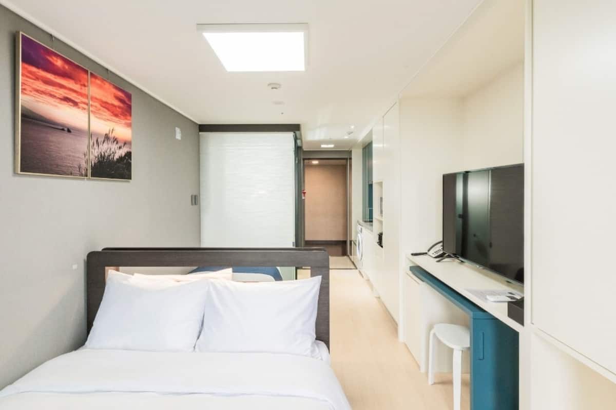 Quarto de hotel com uma cama, uma televisão, uma escrivaninha e um quadro na parede.