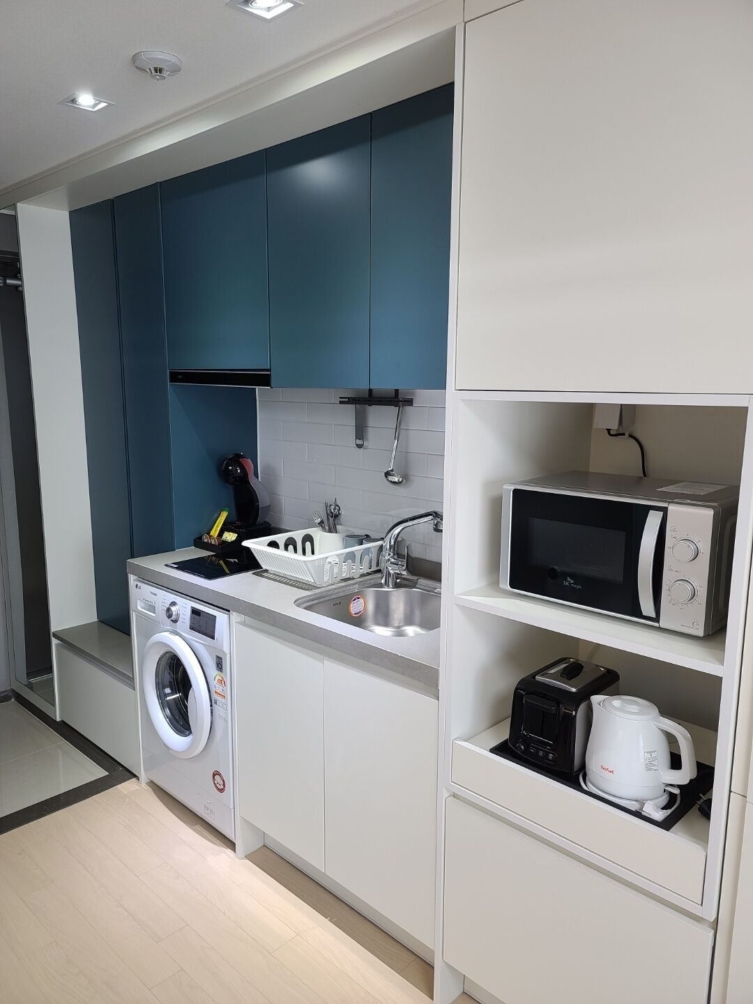A compact kitchen with a washing machine, a microwave, and a toaster.