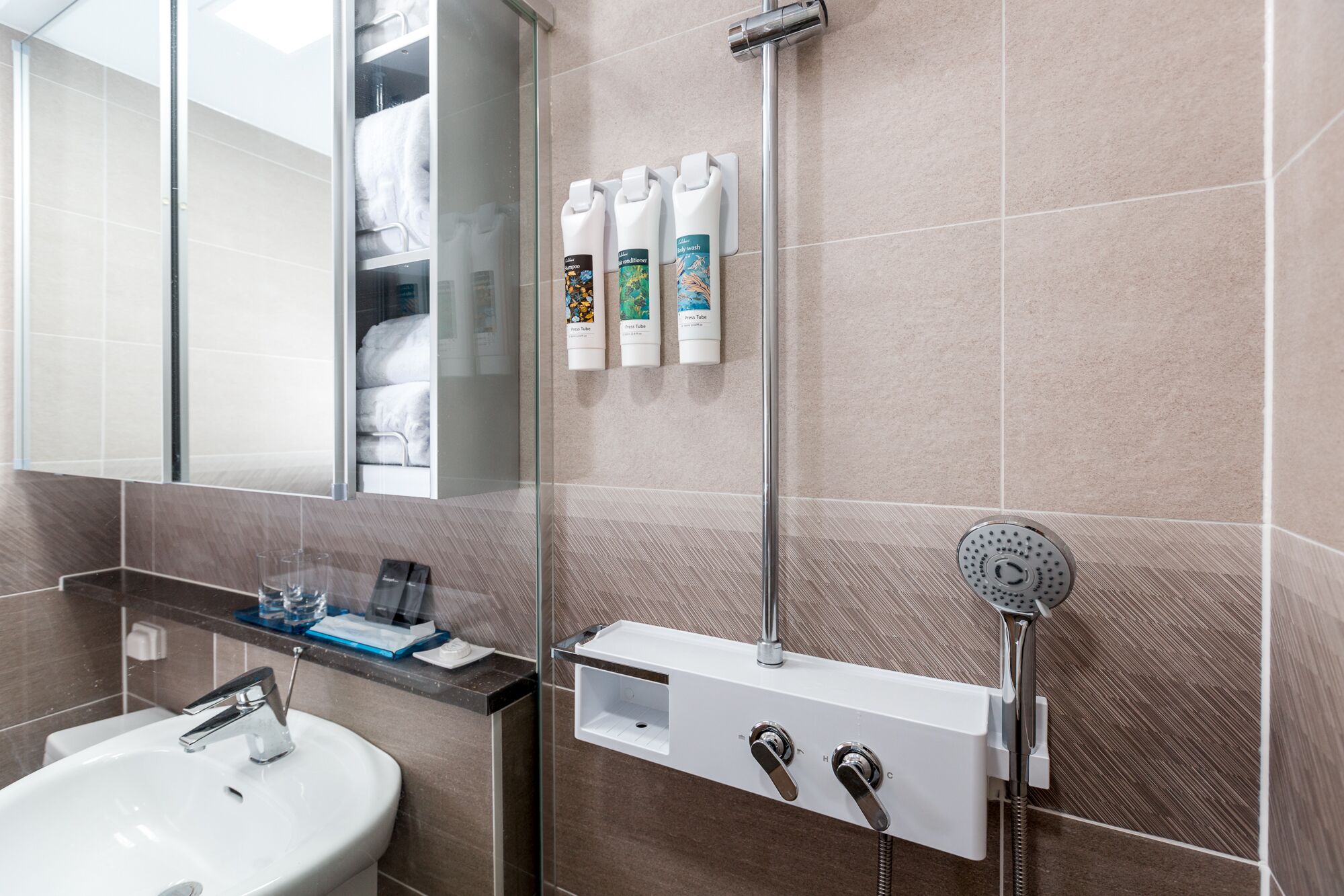 A modern bathroom with a glass shower enclosure, a built-in sink, and a towel rack with toiletries.