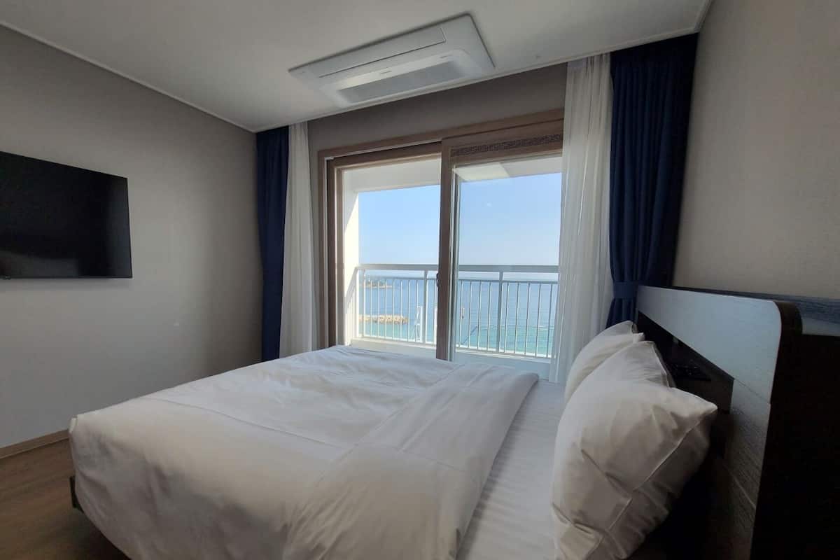Quarto de hotel com cama grande, televisão na parede e varanda com vista para o mar.