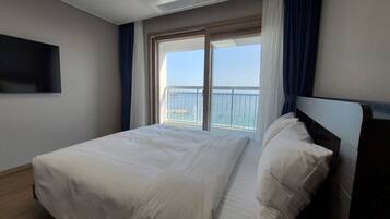 Habitación de hotel con una cama grande, un televisor en la pared y un balcón con vistas al mar.