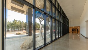 A modern building with a glass facade, a polished interior floor, and a view of outdoor trees and a sculpture. - Risen Oceanpark Hotel (Sokcho)