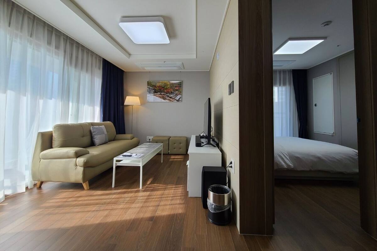 Quarto de hotel moderno com sofá, uma mesinha, televisão, cama e lixeira.