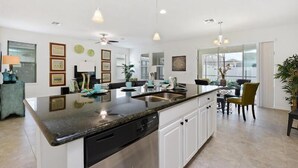 A modern kitchen with a granite countertop, white cabinetry, and pendant lighting.