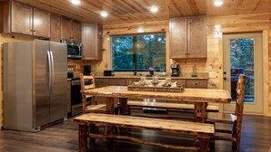 A rustic kitchen with wooden cabinets, a stainless steel refrigerator, a granite countertop, and a wooden dining table with benches. - New! “WaterTastic” Private Cabin heated Indoor Pool, Theater, fantastic view  (Gatlinburg)