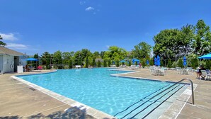 A rectangular swimming pool with clear blue water, surrounded by a concrete deck and shaded by blue umbrellas. - 3 Mi to Boardwalk: Family Bethany Beach Home (Frankford)