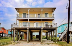 Residential building elevated on stilts, featuring a flat roof and balcony with white columns.