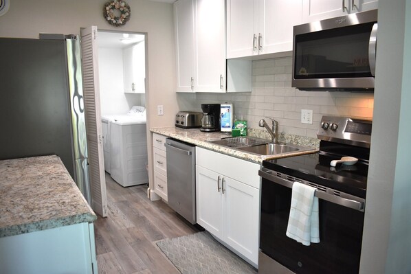 A compact kitchen with white cabinets, a stainless steel microwave, a built-in oven, and a dishwasher.