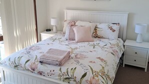 Ein Schlafzimmer mit einem Bett, zwei Nachttischen, einem Deckenventilator und einem Fenster mit Jalousien.