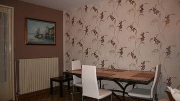 A dining area with a table and chairs, a radiator, a floral wallpaper, and a painting on the wall.