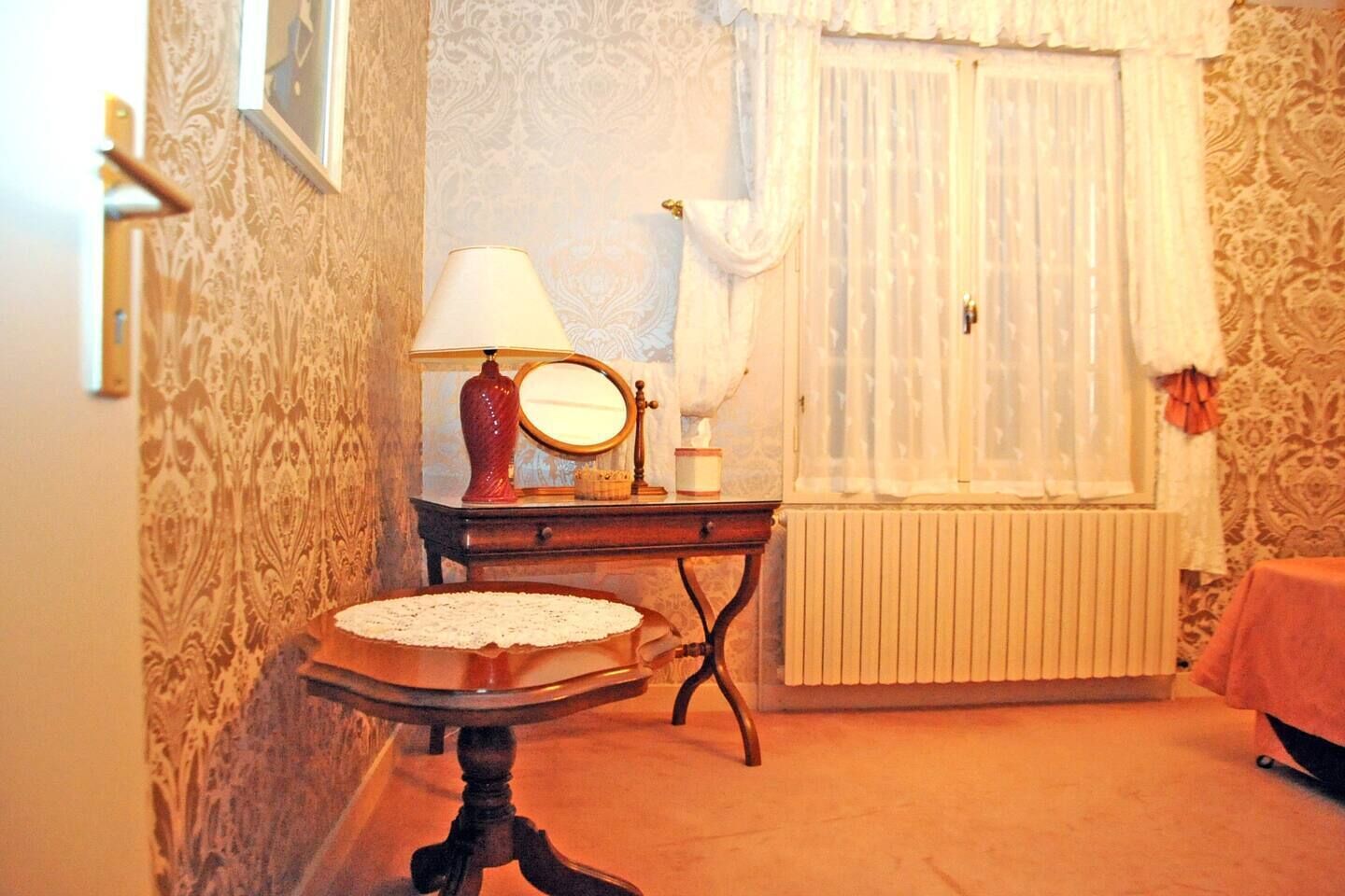 Een kamer met een lamp in vintage stijl, een spiegel, een klein tafeltje en een radiator.