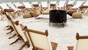 Una spiaggia con file di sdraio di legno e un barbecue nero sulla sabbia.