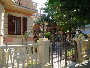 A residential building with a gated entrance, a balcony, and a garden area with potted plants. - Petit Chateau - Room with kitchen (Montecatini Terme)