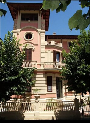 Un bâtiment rose doté d’un balcon, d’une fenêtre ronde et d’une porte.